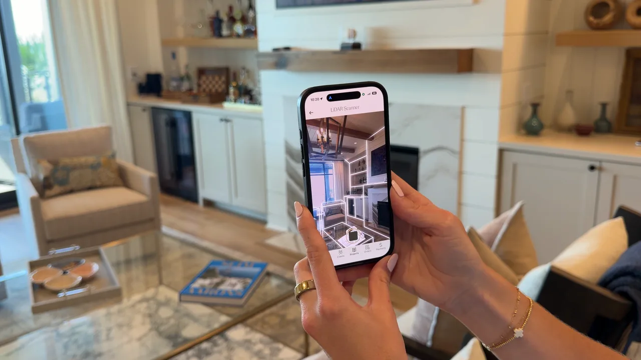 A designer holds up a phone running the LiDAR room scanner, which overlays a glowing wireframe of the living room onto the camera view in real time.
